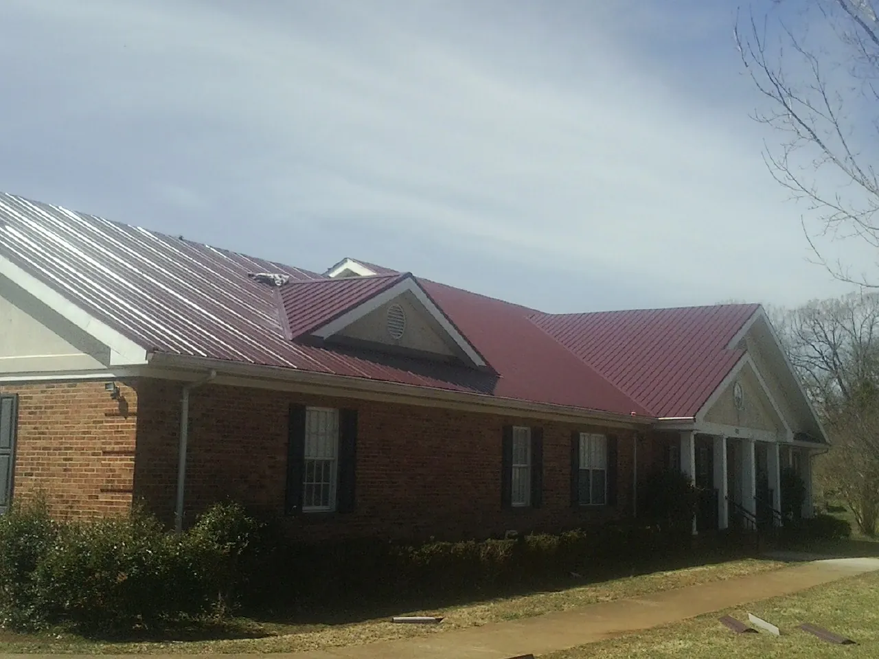 Red metal roof with gabled entries on a long brick building, from a Hail Damage Roof Repair job in Slaterville Springs