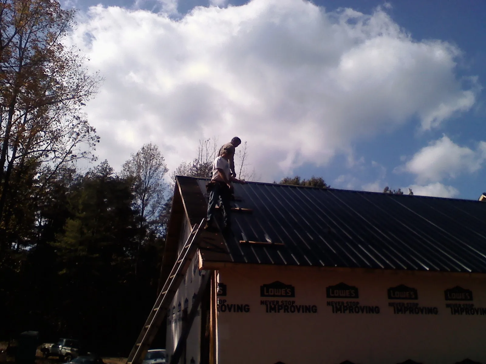 Roofer fastening dark metal panels high against a cloudy sky, from a Roof Inspection job in Slaterville Springs