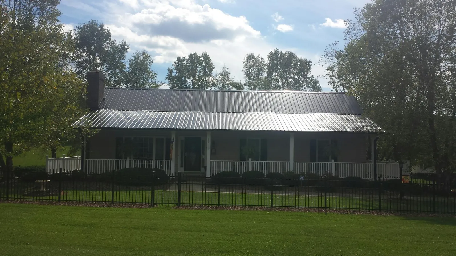 Gray metal roof on a brick ranch with a full width front porch — Gutter Guard Installation work by our crew in Slaterville Springs
