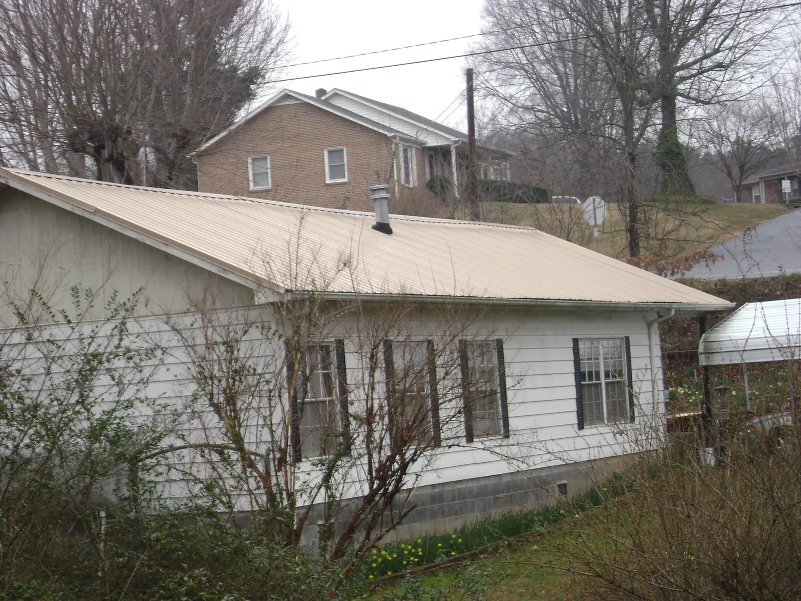 Tan metal roof on a white sided house set into a hillside — Commercial Roofing by Roofing Brothers in Slaterville Springs